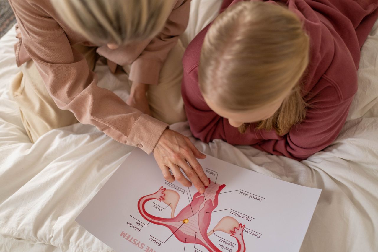 Mother and daughter studying reproductive system illustration for sex education at home.